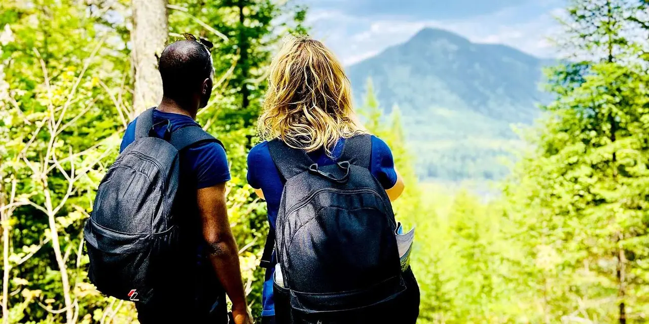 Two hikers with backpacks looking out over forested mountains