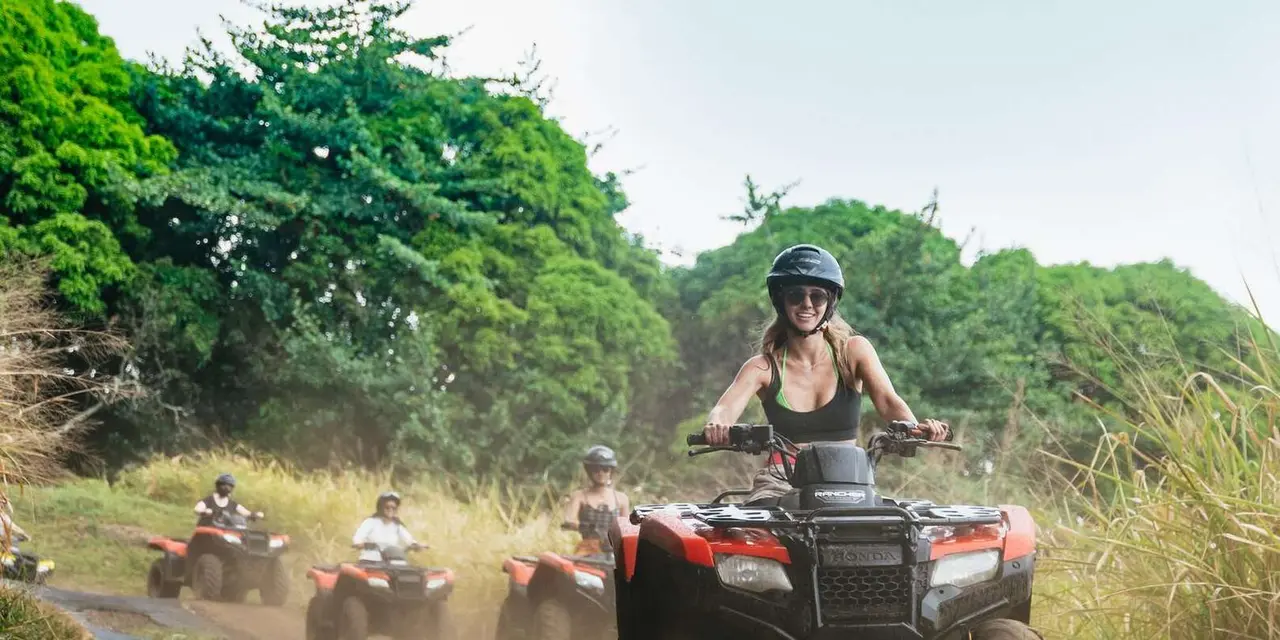 Riders in helmets on ATVs kicking up dust on a red-dirt track through dense green jungle