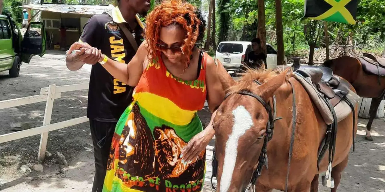 A woman in a green, yellow and red dress holding a brown horse beside a man in a Jamaica shirt