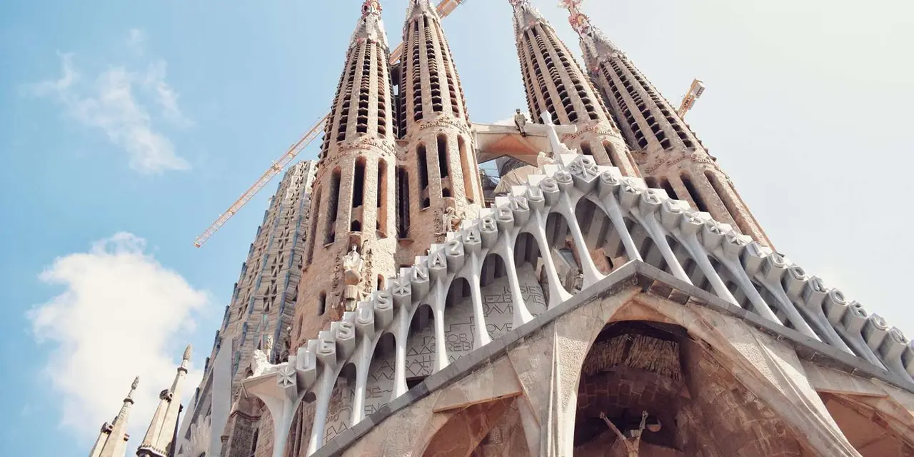 Looking up at the Sagrada Família's spires and the white Passion facade lettering against a pale blue sky