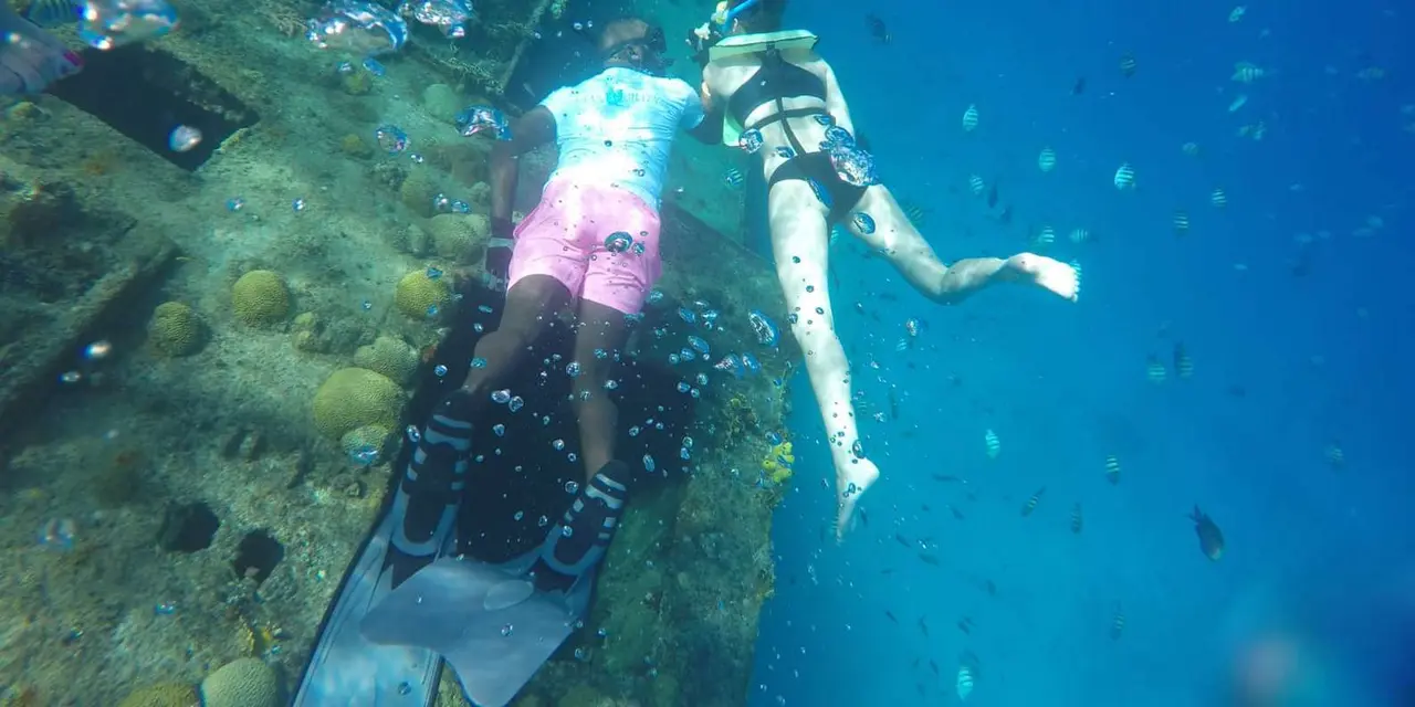 Two snorkelers diving beside a wreck in clear blue water