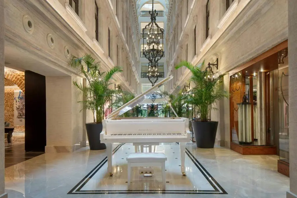 Marble atrium of JW Marriott Istanbul Bosphorus with a white grand piano, potted palms and a tall chandelier under the skylight