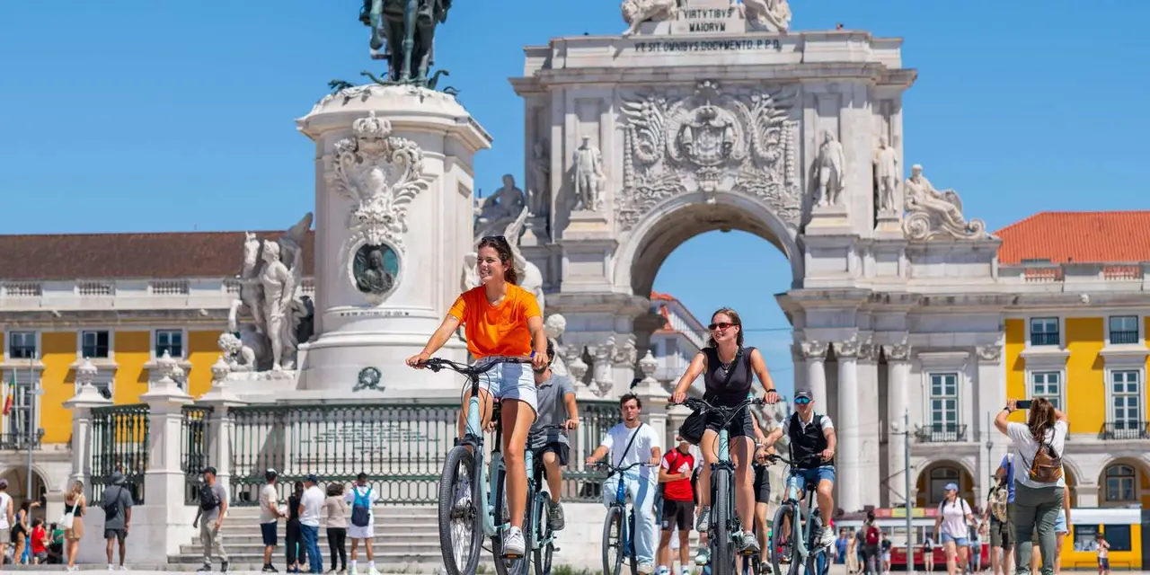 A group of cyclists riding across Praça do Comércio in front of the triumphal arch and the equestrian statue