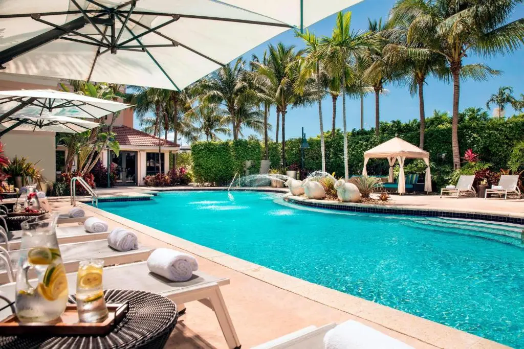The pool at the Renaissance Fort Lauderdale hotel, with lounge chairs, white umbrellas, a cabana and palm trees under a blue sky