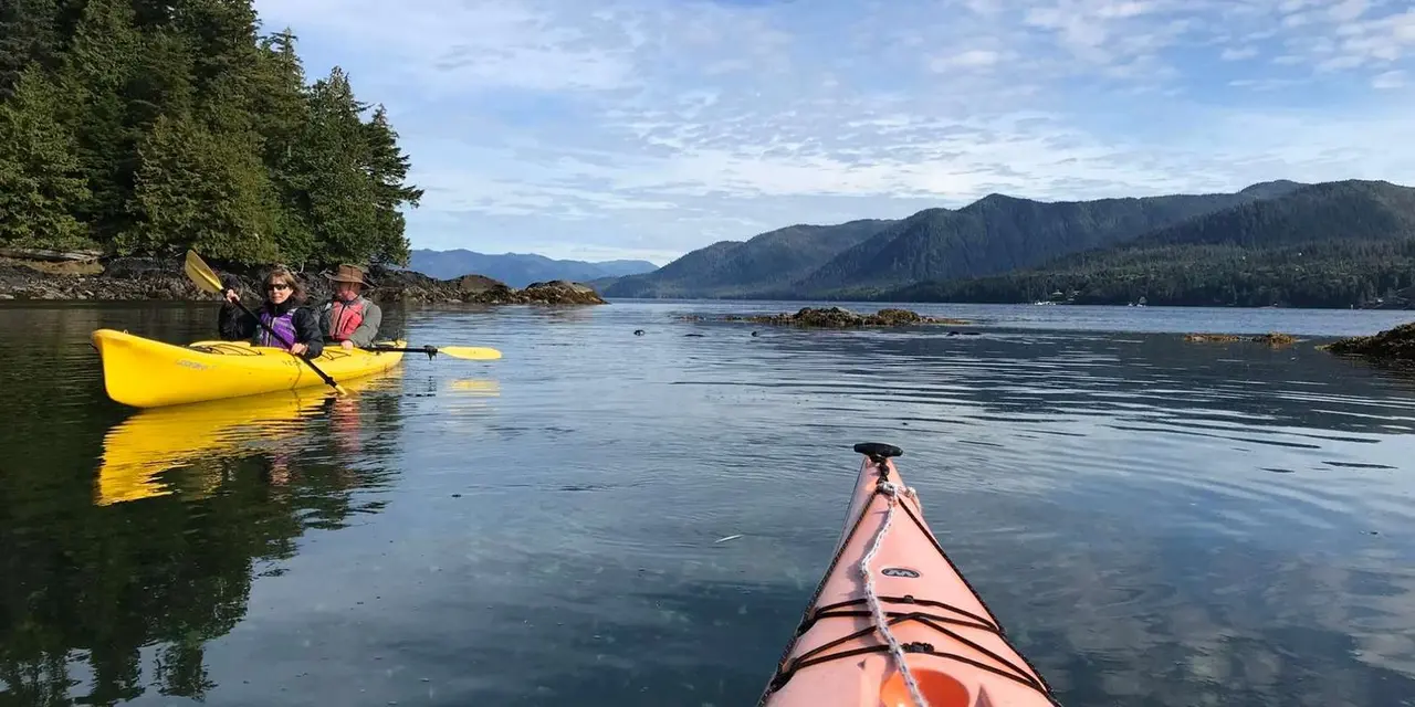Yellow kayaks on calm water below forested hills