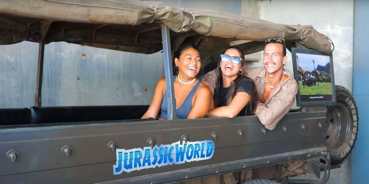 Three laughing passengers in an open-air safari vehicle marked Jurassic World