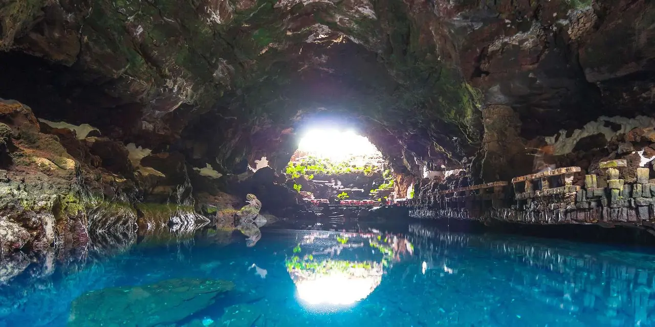A clear turquoise pool inside a dark lava cave with daylight at the far opening