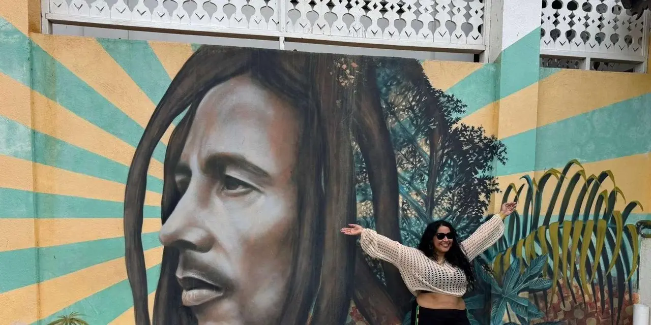 A woman posing in front of a large mural of Bob Marley