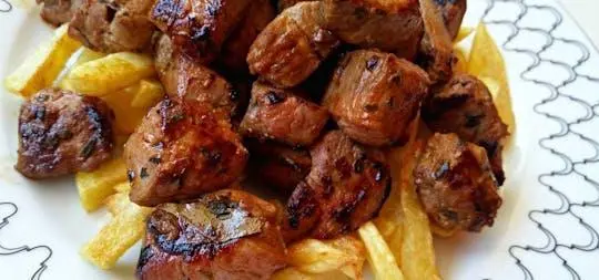 A plate of browned, grilled meat chunks served on a bed of fries