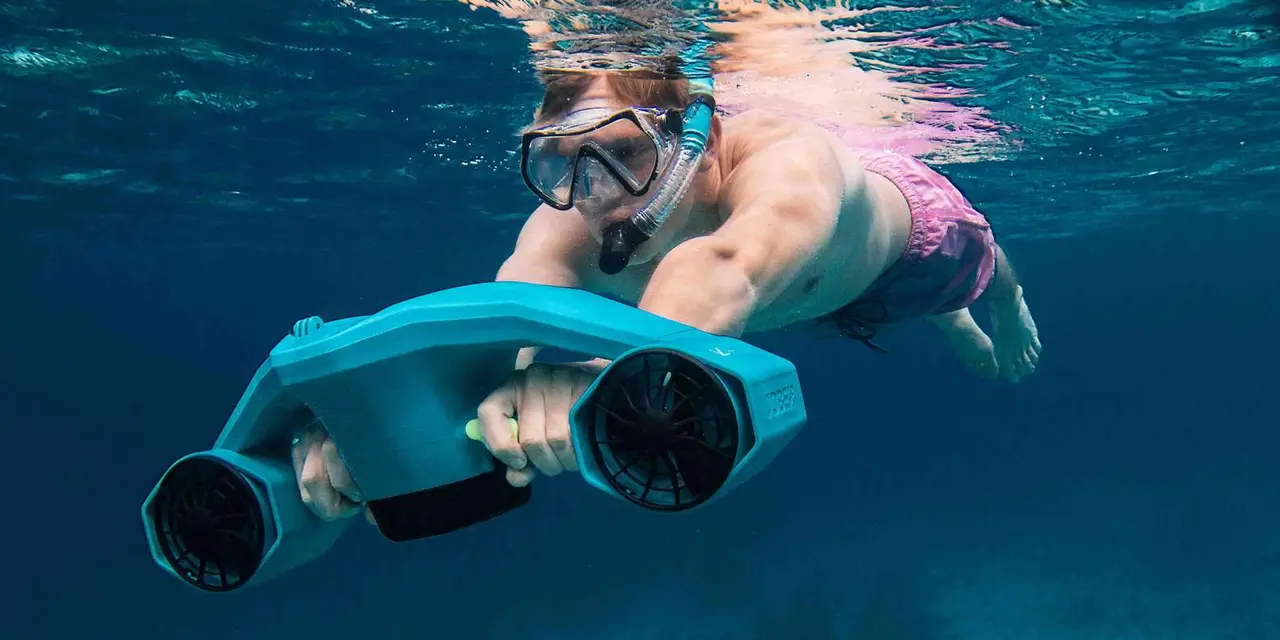 A snorkeler holding a turquoise sea scooter underwater in deep blue water