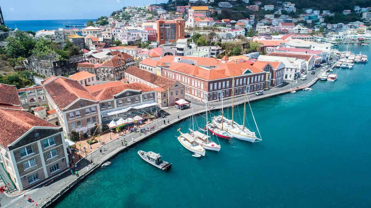 St. George's Carenage from above: red-roofed Georgian buildings curving around a turquoise harbor with sailboats moored along the quay