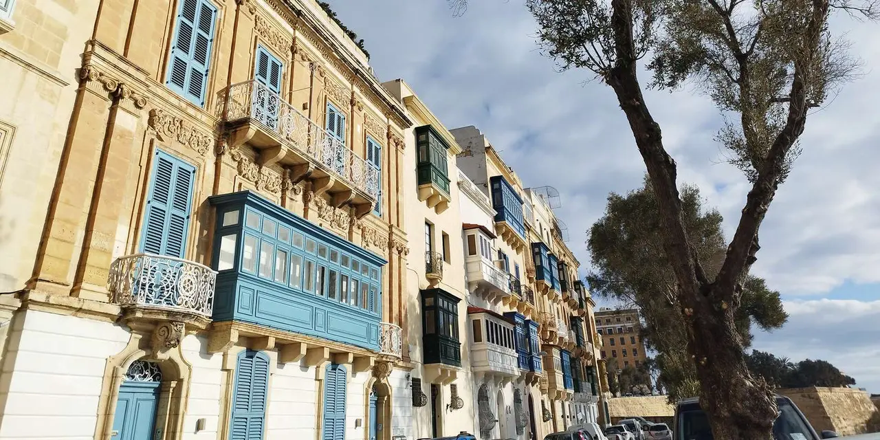 A narrow Valletta street of honey-coloured stone houses with painted wooden balconies