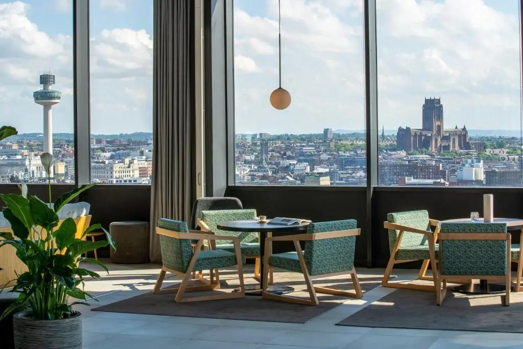 INNSiDE Liverpool's lounge, with green armchairs by tall windows looking out over the city to Radio City Tower and Liverpool Cathedral