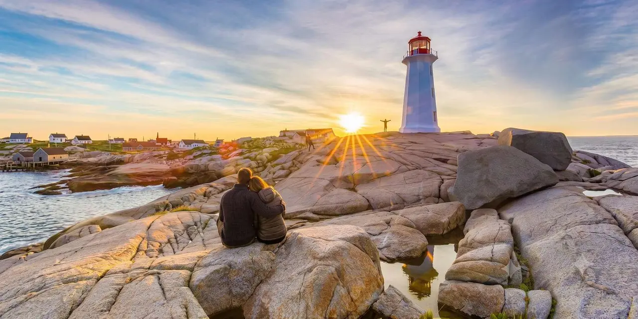 A person sitting on smooth granite rocks above the sea at Peggy's Cove at sunset