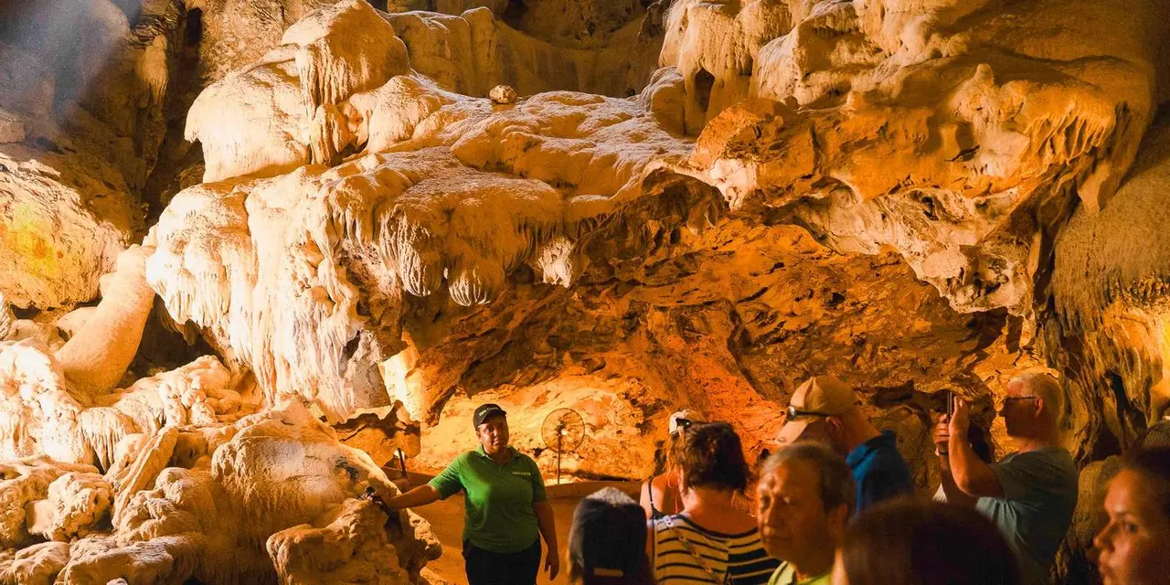 A guide leading a group through an orange-lit limestone cave with dripping rock formations