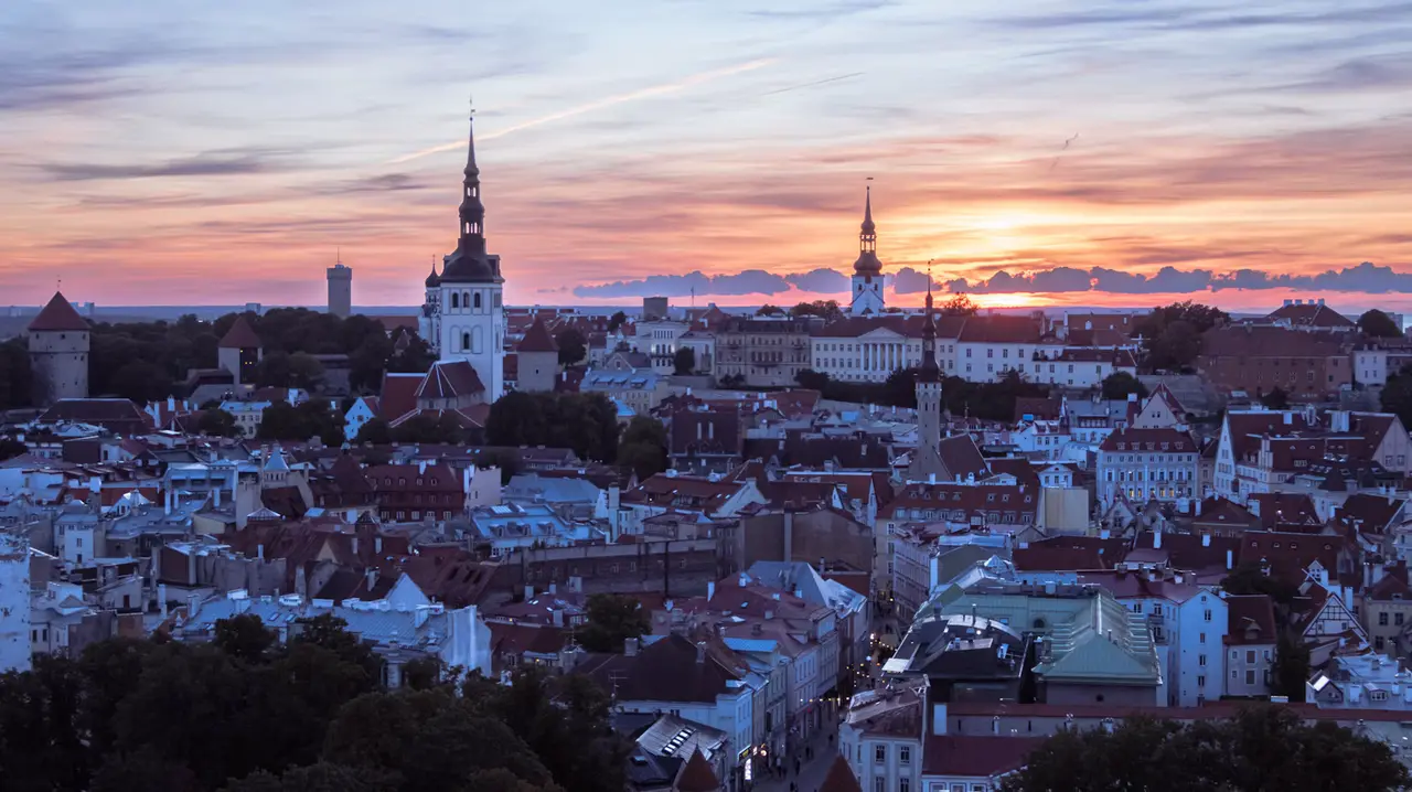 Sunset over Tallinn's Old Town, with red-tiled rooftops, church spires and medieval towers under an orange and purple sky