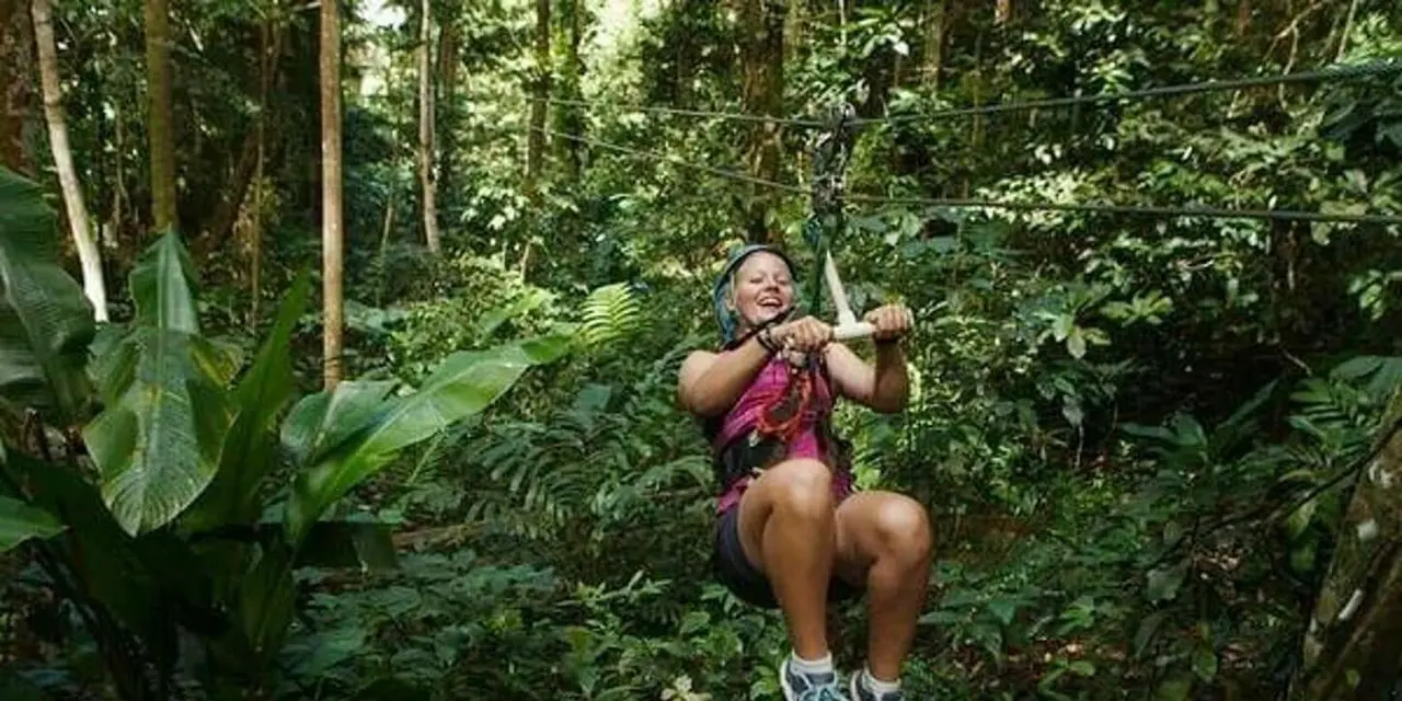 A woman in a pink top riding a zip line through green rainforest
