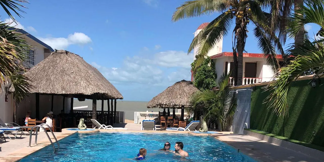 A blue swimming pool with swimmers, thatched shades and palm trees