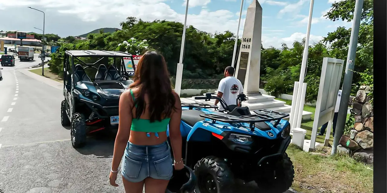 A woman in denim shorts and a teal top beside a purple ATV, with a stone obelisk monument behind