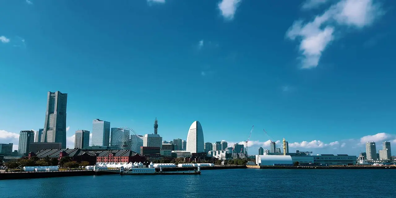Yokohama's Landmark Tower, the Cosmo Clock 21 ferris wheel and the Red Brick Warehouse seen across blue harbor water under a clear sky