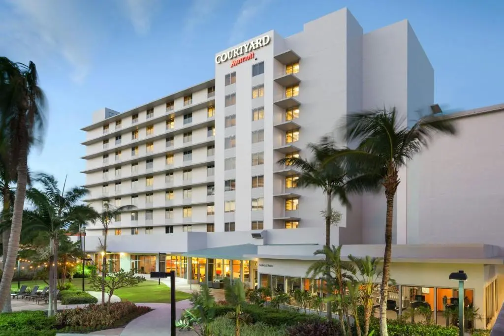 The Courtyard Miami Airport tower lit up at dusk behind palm trees and a landscaped walkway