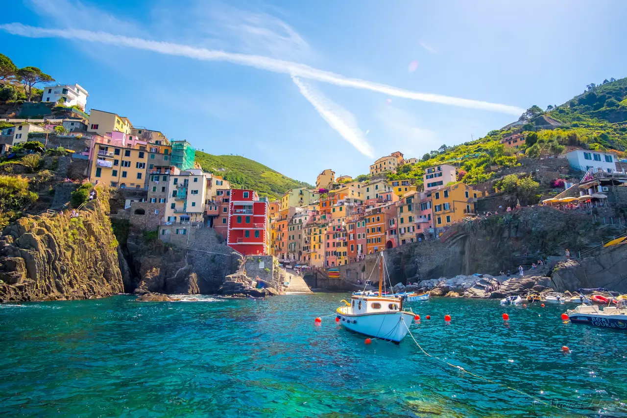 Riomaggiore's pink, red and yellow houses stacked above its little harbour, with a boat on turquoise water: the nearest Cinque Terre village, about 10 minutes by train from La Spezia