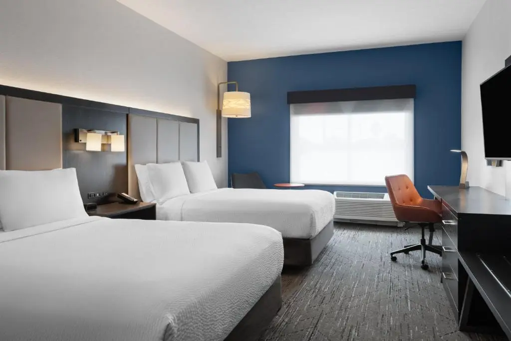 A Holiday Inn Express guest room with two made-up queen beds, a blue accent wall and a desk with an orange chair