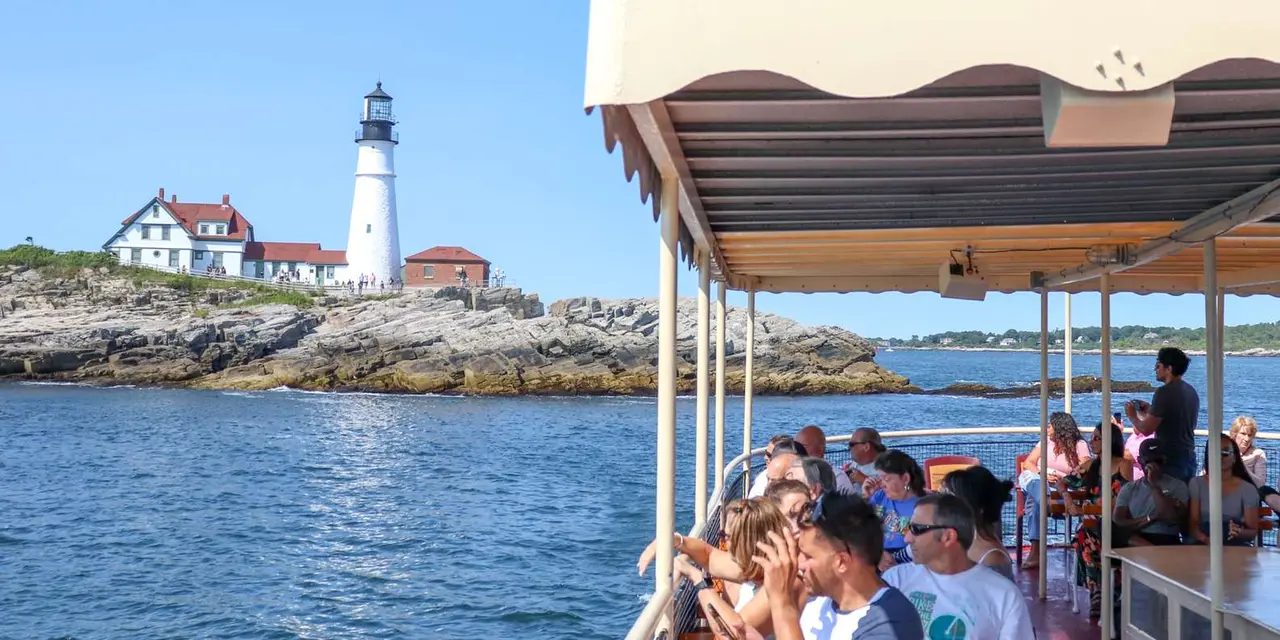 Portland Head Light on its rocky point, seen from under the covered deck of a sightseeing boat with passengers on board