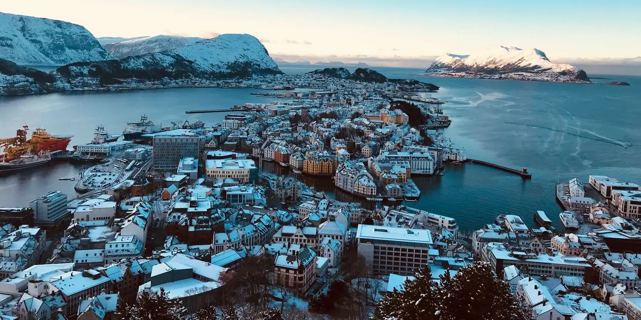A wintry view over Ålesund's rooftops and harbour with snowy mountains on the horizon