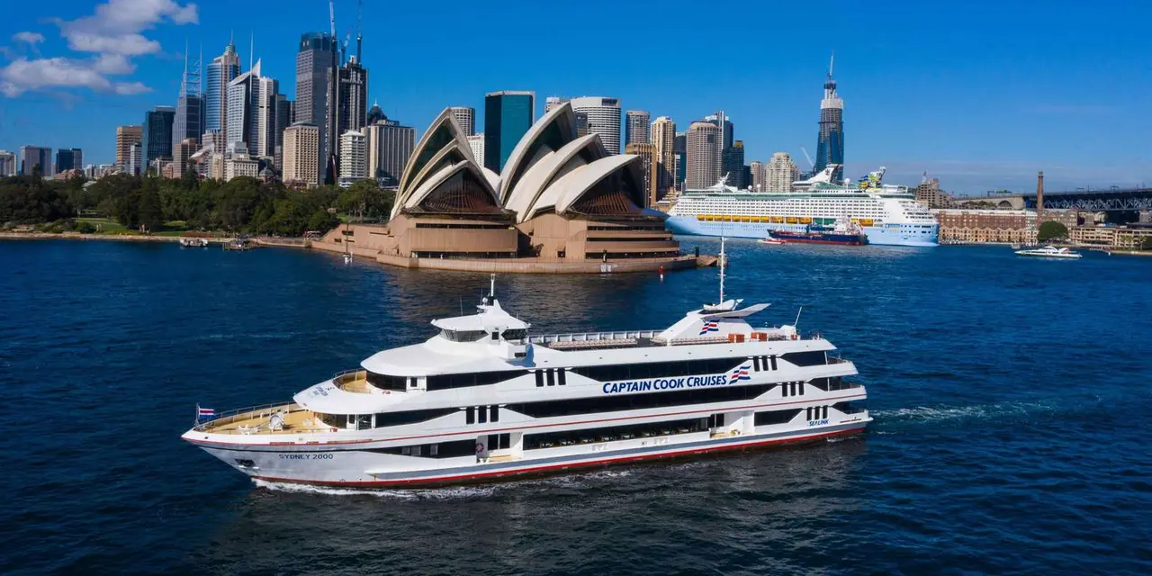A white cruise vessel on the harbour with the Opera House and city skyline behind it