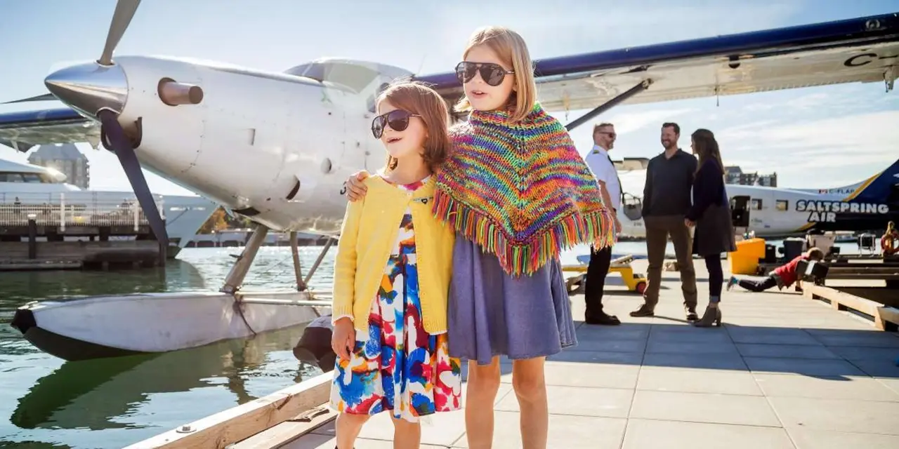 A girl in a striped poncho on a seaplane dock, with passengers boarding a floatplane behind her