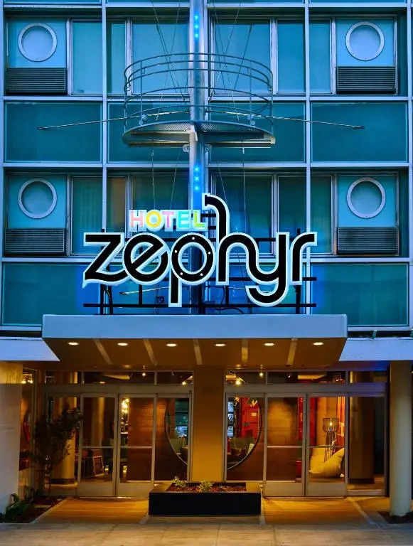 Hotel Zephyr's entrance at dusk, with its blue-lit sign over the glass doors and porthole windows above
