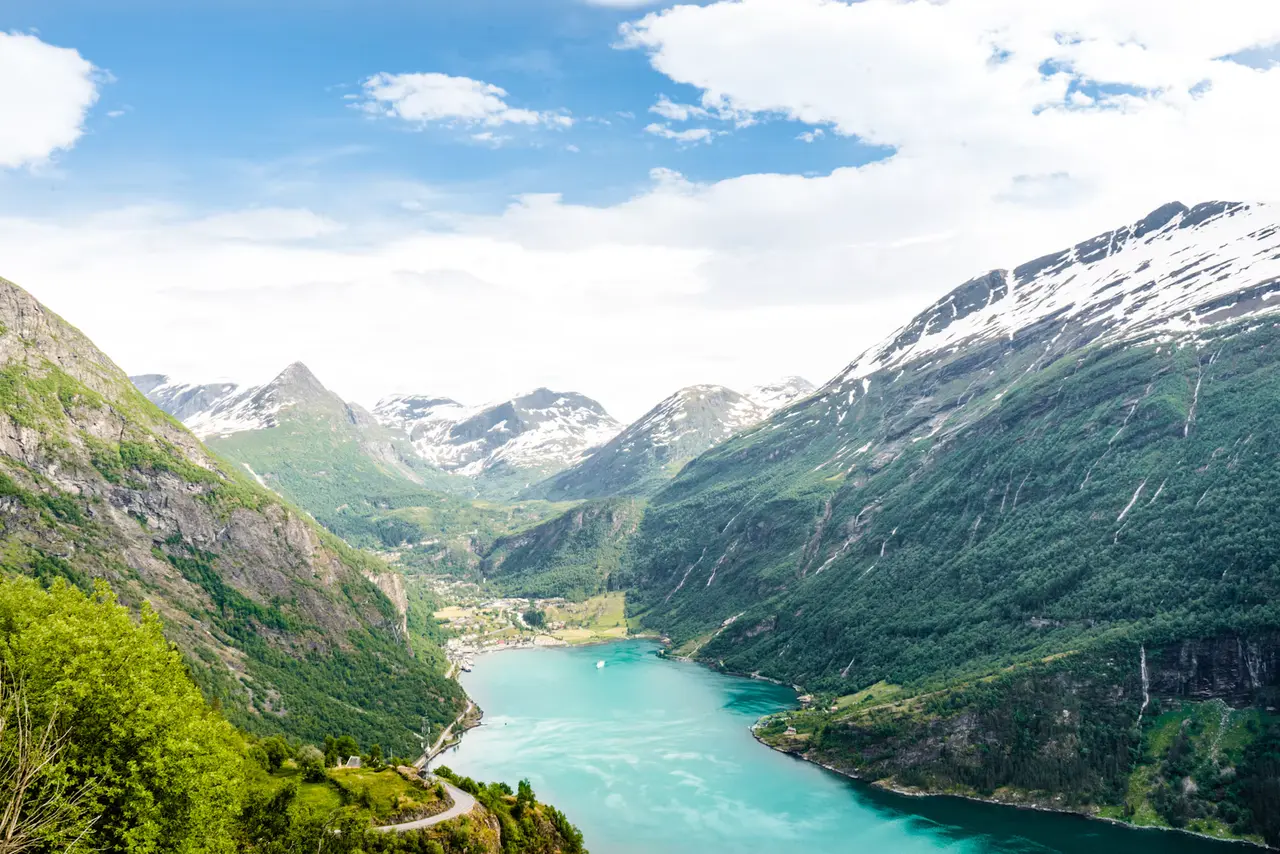 The turquoise Geirangerfjord winding between steep green mountains and snow-streaked peaks, seen from high above Geiranger village