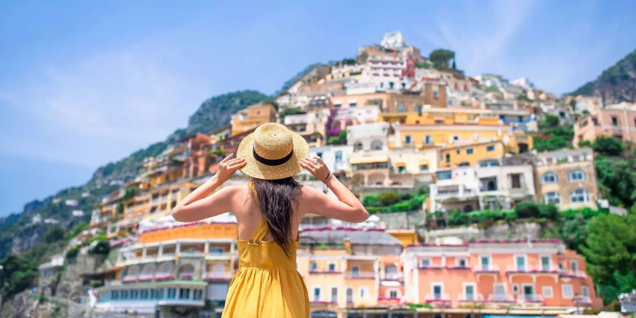 A woman in a straw hat looking out over Positano's houses stacked up the hillside