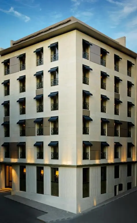 Corner facade of Witt Istanbul Suites, a pale stone building with dark window awnings, under a blue evening sky