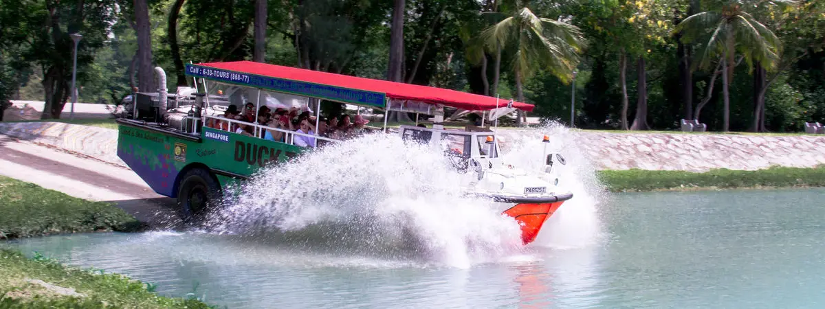 A DUCKtours amphibious vehicle with a red canopy splashing into the water with passengers aboard