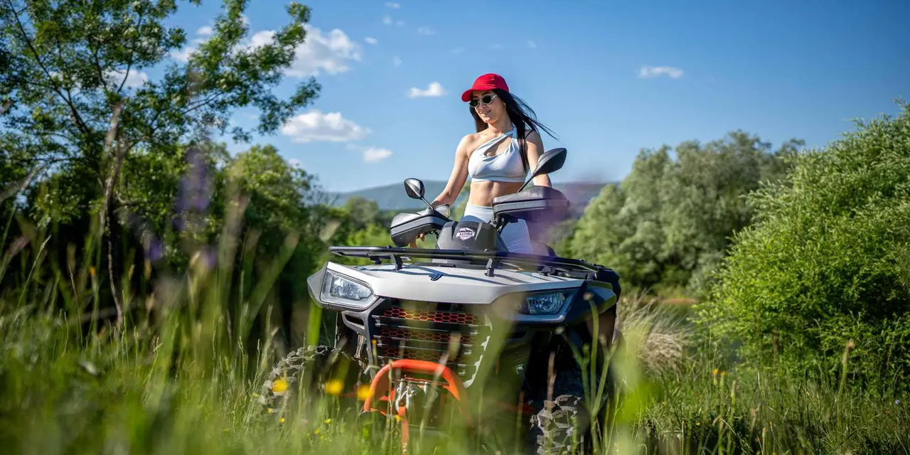 A rider in a red cap on an orange quad bike in green grass under a blue sky