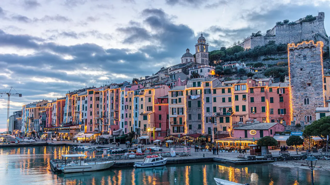 Portovenere's tall pastel harbour houses and moored boats under a cloudy sky
