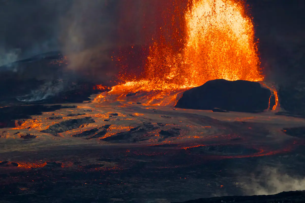 A fountain of orange lava erupting from a vent in Kīlauea's crater, with smoke over the dark crater floor