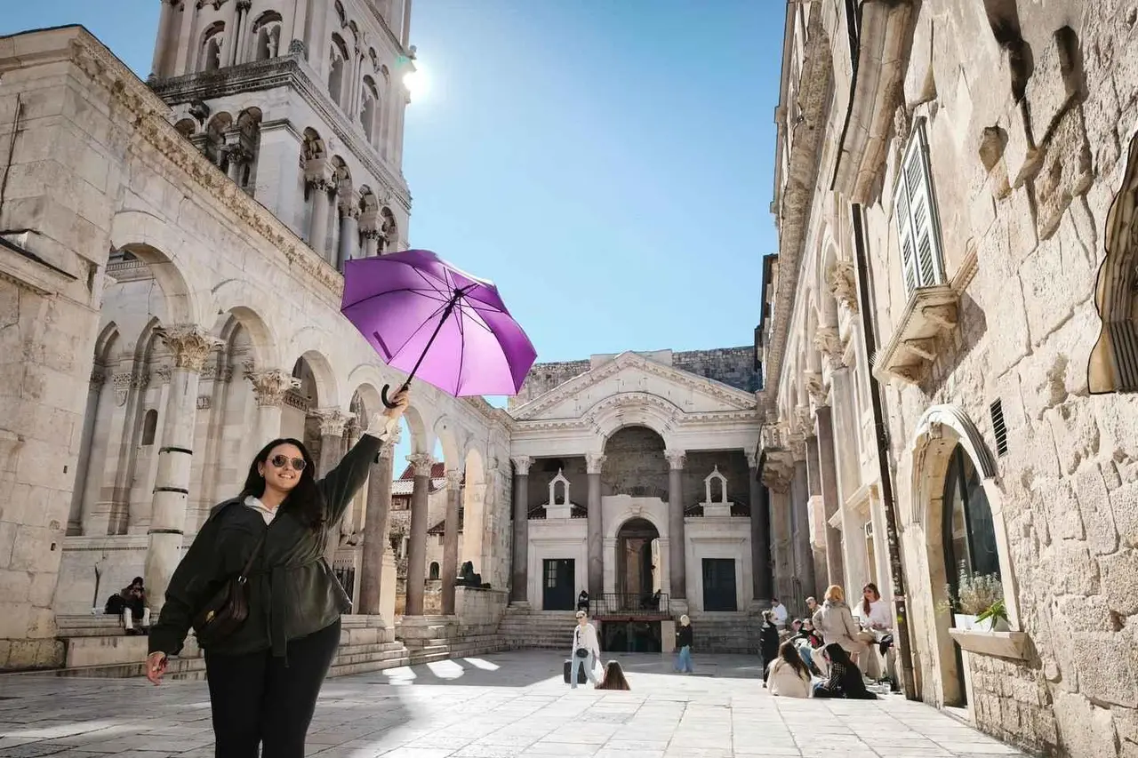 A guide holding up a purple umbrella in the Peristyle of Diocletian's Palace, with the cathedral bell tower behind