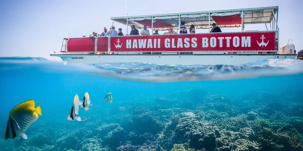 A split view of the red-signed Hawaii Glass Bottom Boats vessel above the waterline and blue water over reef below