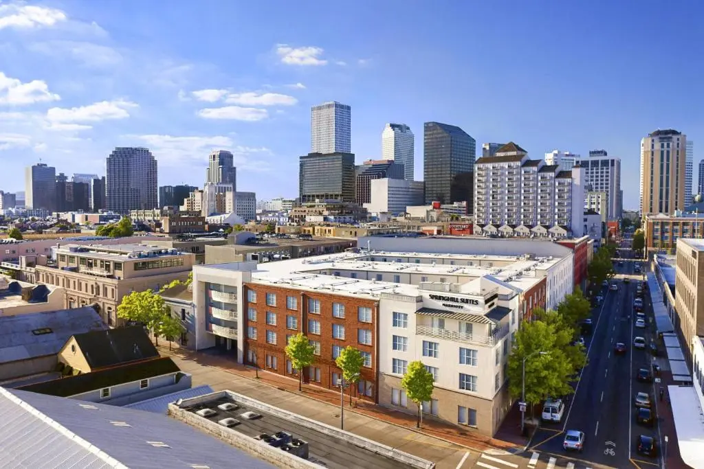 Aerial view of the brick SpringHill Suites building on a Warehouse District street corner, the downtown New Orleans skyline behind under a blue sky
