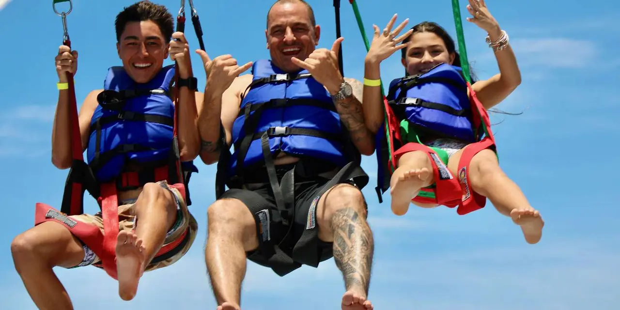 Two smiling men in life jackets hanging in a parasail harness against a blue sky