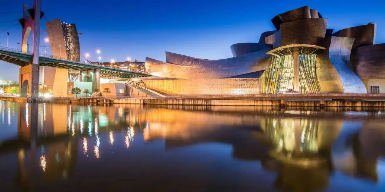 The Guggenheim Museum's curved titanium walls lit gold at dusk beside a river and a red bridge