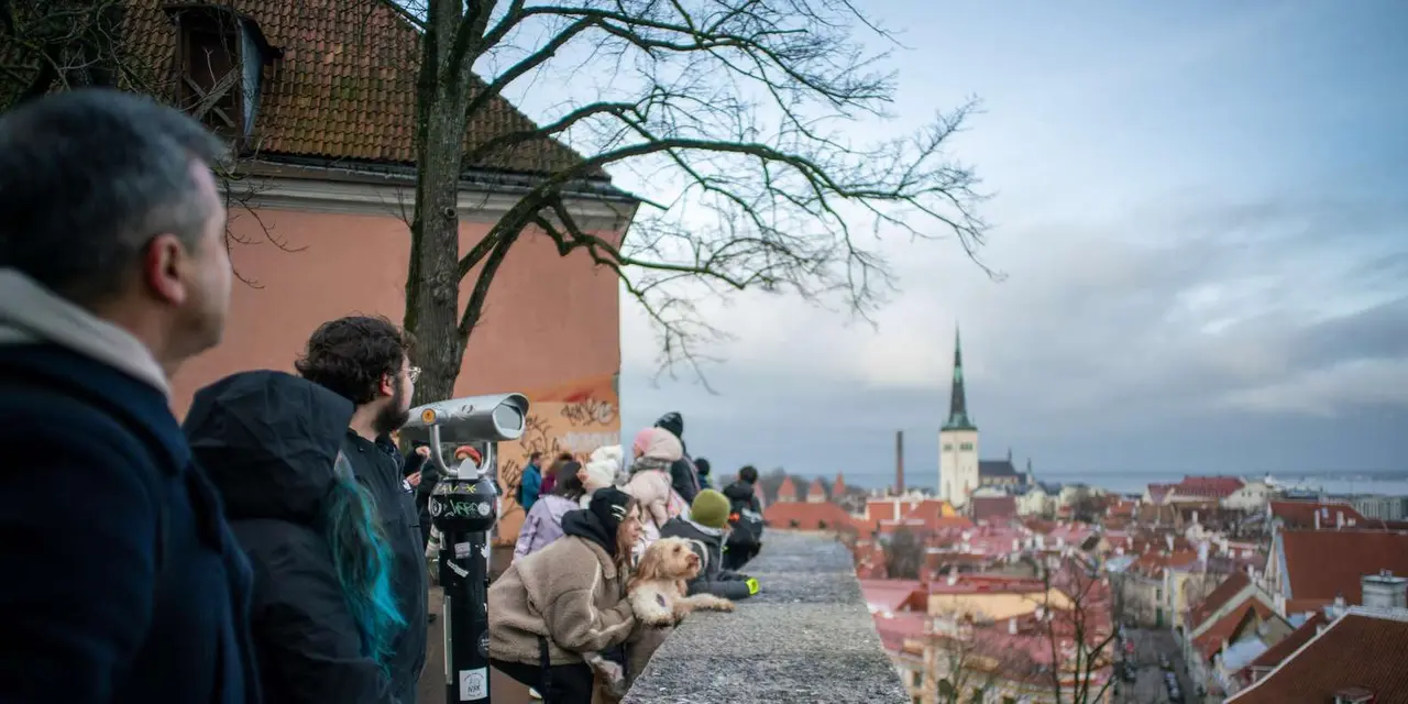 Tourists at a hilltop viewing platform in Tallinn looking out over red rooftops and the green spire of St. Olaf's Church