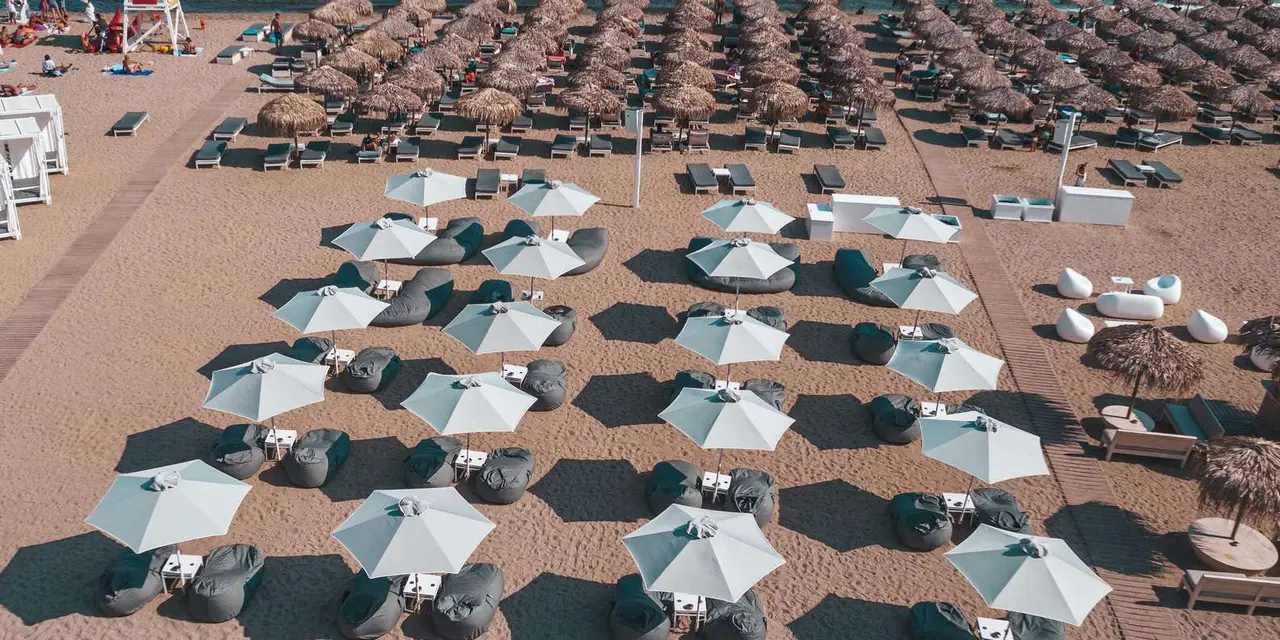 Aerial view of rows of white umbrellas and loungers on a sandy beach beside turquoise water