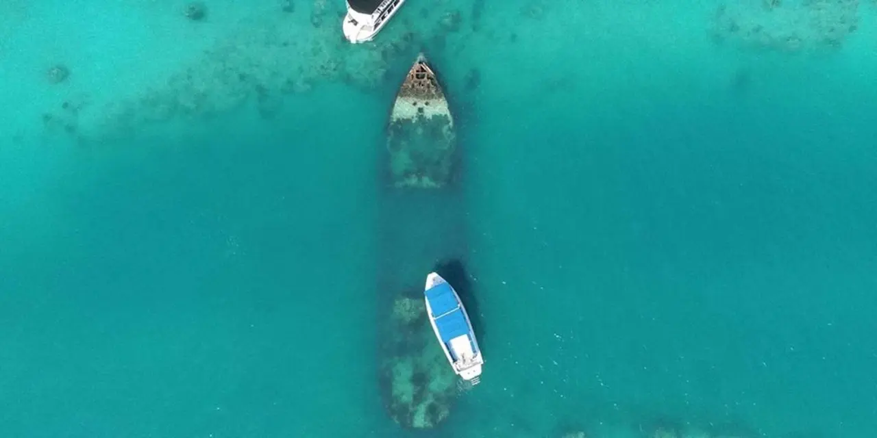 Aerial view of two small boats over a shipwreck visible through shallow turquoise water