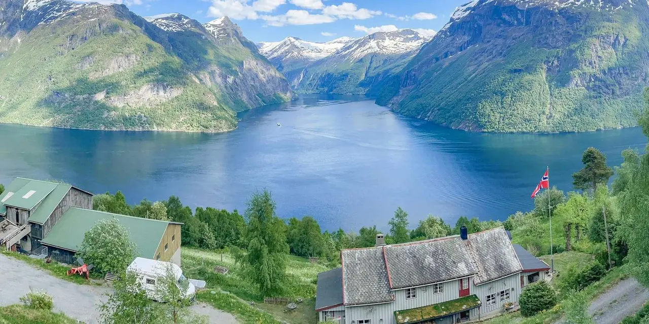 A green fjord valley under snowy peaks, with farm buildings in the foreground