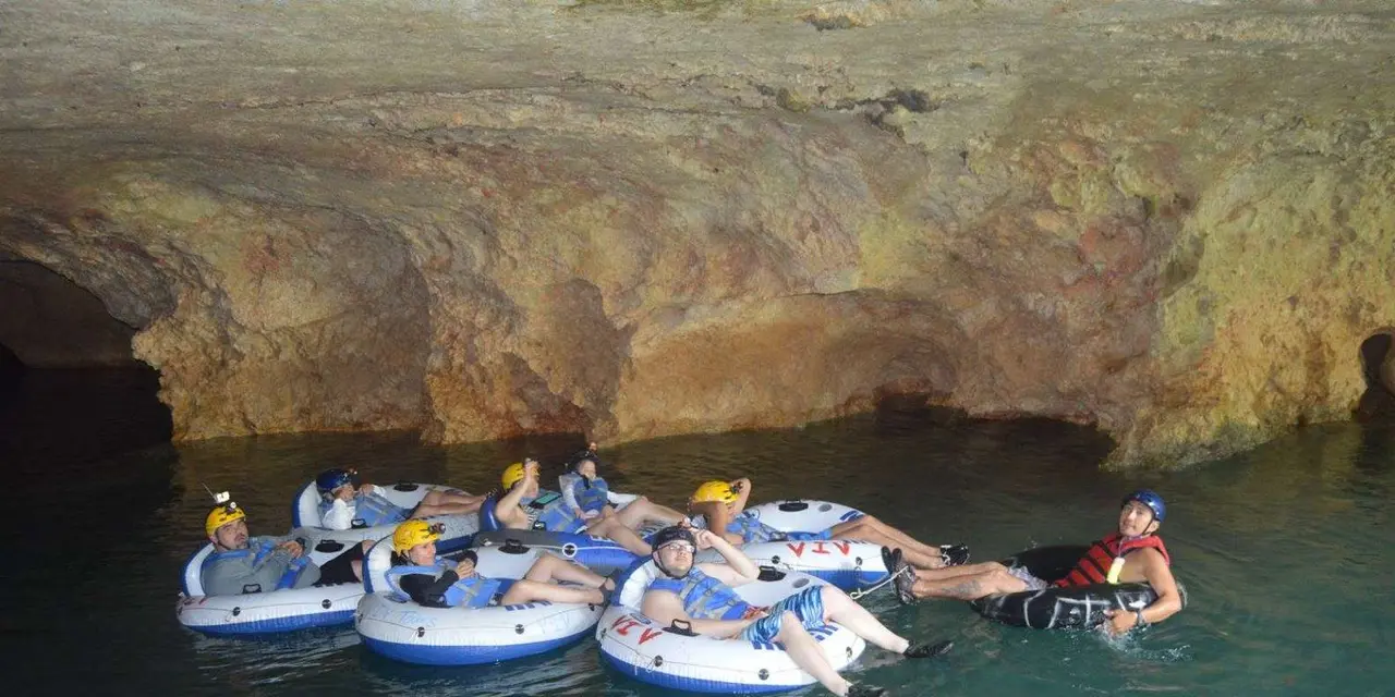 A line of people in white tubes linked together at the mouth of a cave