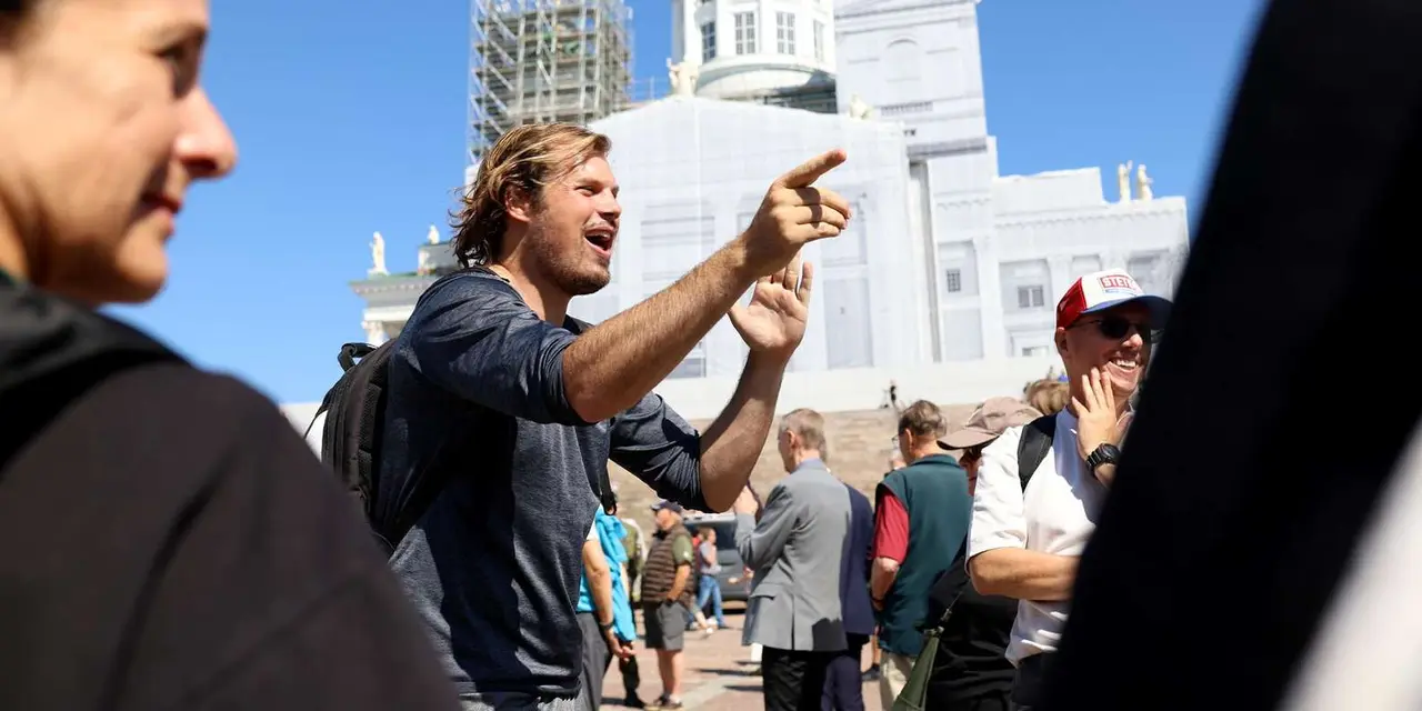 A tour guide in a dark shirt gestures to a group on a sunny day, with the white walls of Helsinki Cathedral behind them